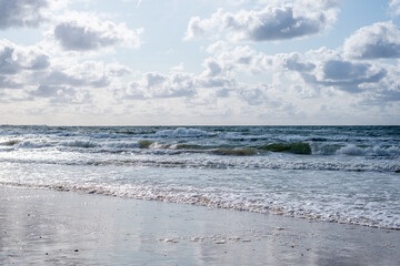 The play of white waves of the sea with clouds in the blue sky.  The rolling sea on a cloudy day.