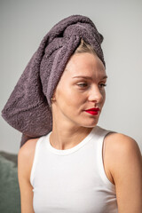 The smiling young woman with red lips and white T-shirt just washed her hair. A dark gray towel on womans head.