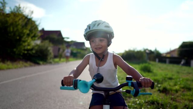 Joyful child riding bicycle outside in sunny beautiful day. One small boy rides bike wearing helmet. Smiling sportive cyclist kid