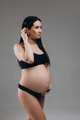 Portrait Of Happy Pregnant Woman In Lingerie With Smile Face Made Of Cream On Her Belly Posing Over Beige Background, Beautiful Young Expectant Female In Underwear Smiling At Camera.