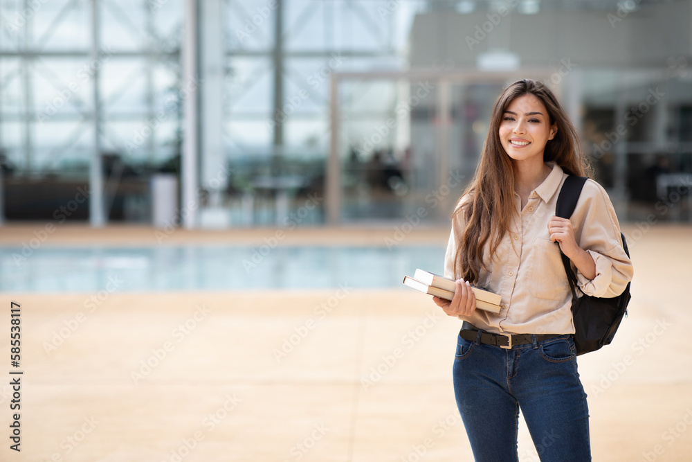 Wall mural happy young european female student in casual with backpack and books go to lesson at university, ou