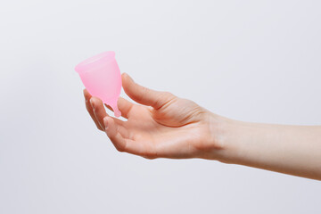 Female hand holding pink menstrual cup on white isolated background. Hygiene products, female...