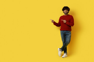 Cheerful young eastern guy pointing at copy space on yellow