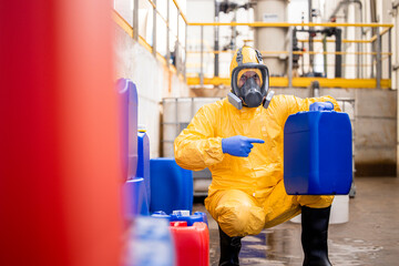 Chemicals production plant worker in protective equipment and gas mask pointing finger to the plastic canister with acid.