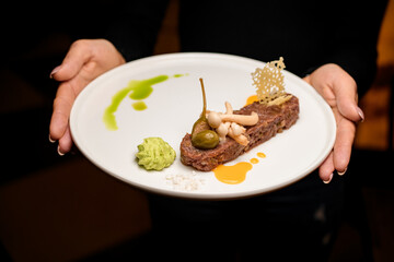 plate with tasty meat tartare appetizer in female hands