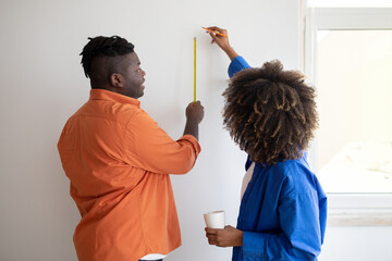 Black young couple with tape ruler taking measurements on white wall