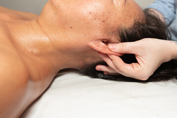 Massage therapist strong hands and thumbs apply accupressure point holds on the patient's ears for...