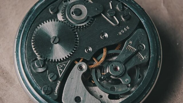 Clock mechanism rotates close-up. Vintage round stopwatch mechanism working in a macro. Old retro clockwork gears, cogwheels, and pendulum movement inside the ancient metal watch.
