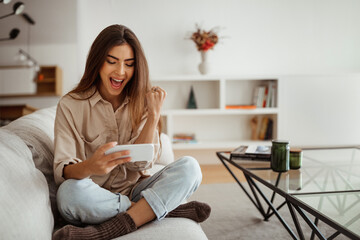 Glad shocked millennial mixed race woman with open mouth looking at phone, reading message, chatting