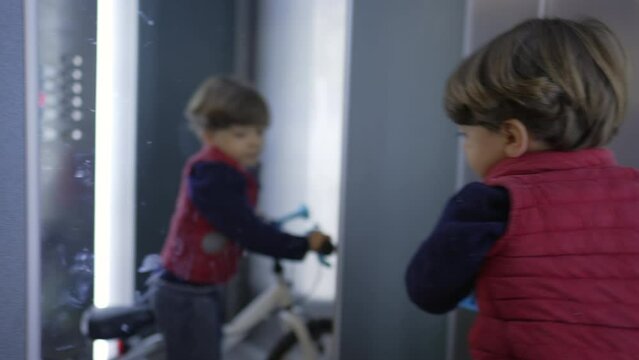 Child inside elevator with bicycle pressing button. Domestic lifestyle of small boy arriving home during weekend activity. Kid Going Up