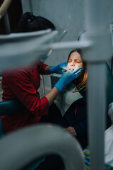 Dentist, doctor woman in rubber gloves with tools diagnoses, treats teeth from caries of a girl, a...