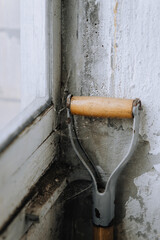 An abandoned, old shovel, garden tool with a wooden handle stands in the corner of the wall of the house. Close-up photography, concept.