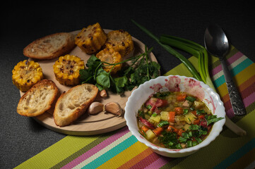 Bowl of pea soup decorated with green onopn, grilled corn, parsley, toasts and garlic