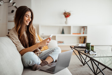 Smiling millennial mixed race woman looks at phone, reads message, has meeting, work with laptop