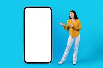Laughing asian woman pointing at smartphone, mockup