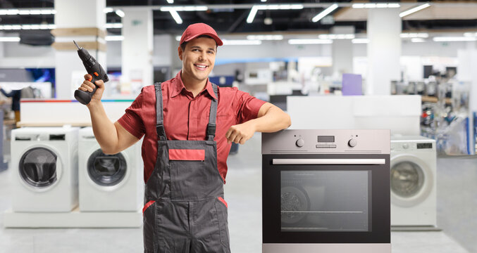 Repairman with an electric drill standing next to an oven in an appliance shop