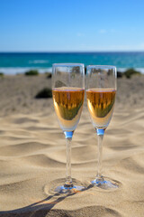 Two glasses of rose champagne or cava sparkling wine served on white sandy tropical beach with dunes and blue ocean, romantic vacation, winter sun on Fuerteventura, Canary, Spain