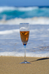 One glass of rose champagne or cava sparkling wine served on white sandy beach and blue ocean water, romantic vacation, winter sun on Fuerteventura, Canary, Spain