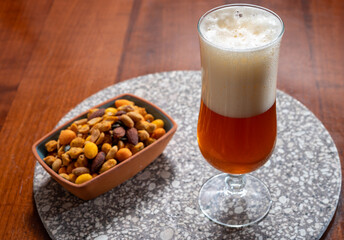 Glass of Belgian light blond beer made in abbey and bowl with party mix nuts