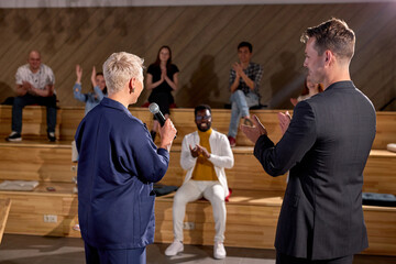 Couch Giving Talk at Business Meeting. Audience in conference hall, clapping hands, greeting new speaker woman with short hair in formal wear, smiling. rear view, copy space. education, management
