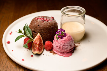 Close-up view of chocolate cake with ice and jar of cream served on white plate