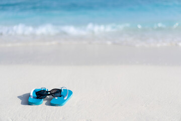 Flip flops and sun glasses on the beach on the background of the ocean in the Maldives.