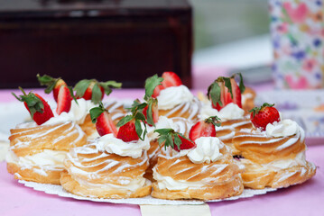Tray full of wreaths with yolk cream on the table of confectionery stand at farmers street food market. Closeup of wreaths with yolk cream and whipped cream, embellished with fresh strawberries.
