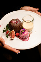 white plate with tasty chocolate cake with ice and jar of cream in female hands