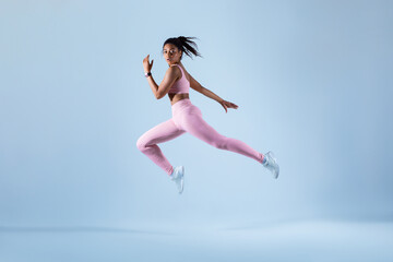 Training concept. Fit black woman in sportswear jumping or running, exercising on neon blue studio background