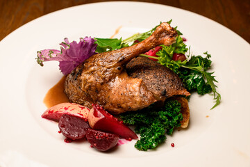 Close-up of roasted duck leg garnished with apples and herbs on plate
