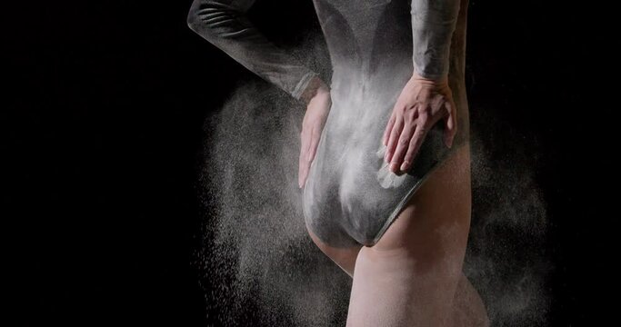rear view on slender slim female booty, woman slapping flour powder on ass, flour is flying around. ballet dancer in black bodysuit after dance, performance. isolated black studio background