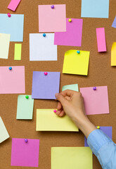 A hand holds a blank sticker for writing ideas on a cork board.