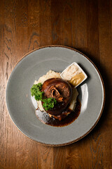top view of tasty fried pork knuckle garnished with herbs on a plate on wooden table
