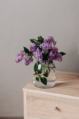 Bouquet of garden lilacs in a glass vase on a wooden bedside table.