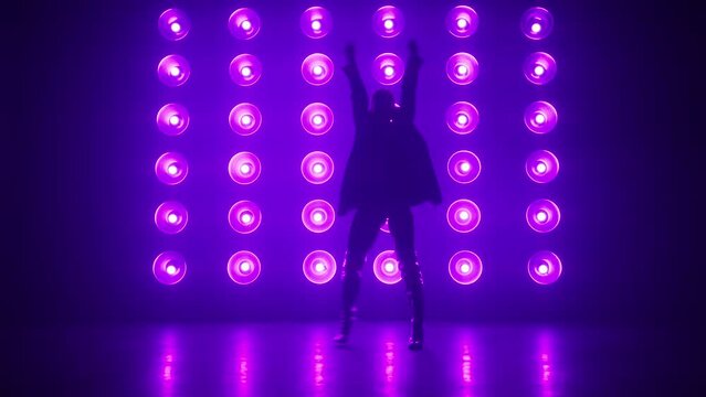 Stylish dancer in trendy outfit performing at concert in Night Club. Night lifestyle, party concept shot. Silhouette of professional RnB dance performer moving hips at bright colorful strobing lights