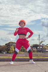 Joven afro de cabello naranja bailando al estilo urbano en parque local con pista de atletismo,...