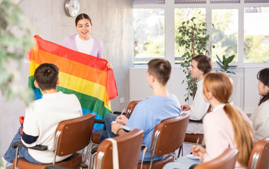 Obraz premium Students sitting at lesson with classmates, listening mature teacher talking about LGBT community and showing rainbow flag