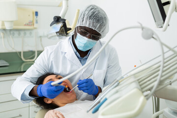 African american dentist professional filling teeth for woman patient sitting in medical chair
