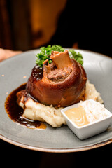 selective focus on fried pork knuckle garnished with herbs with sauce on a plate