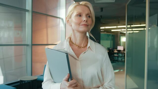 Confident business woman 40s 50s walking in business office hallway. Smiling independent mature female CEO executive enjoying successful corporate career. 4k footage slow motion modern loft office
