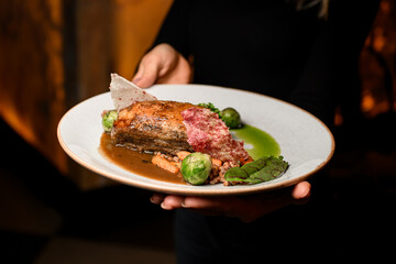 Close-up view on plate with piece of baked pork meat with buckwheat and vegetables in female hands