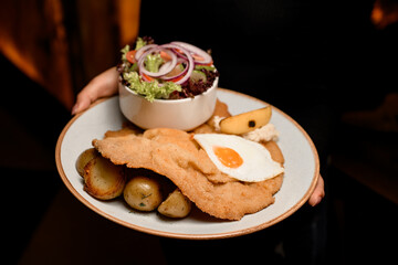 great view on plate with chop with roasted egg and potato and salad in female hands