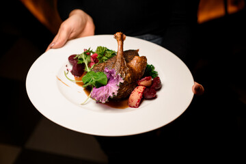 Close-up of roasted duck leg garnished with apples and herbs on plate in female hand