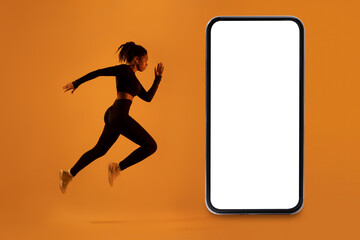Workout application. Fit african american lady exercising near big cellphone over neon orange background, mockup