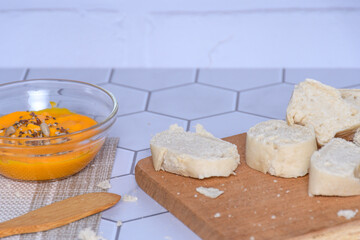 Close-up of a glass container with homemade carrot mayonnaise, bread and spread.
