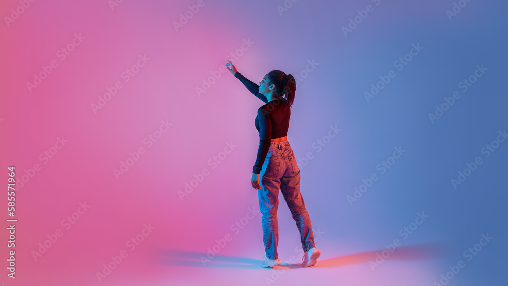 Poster back view of young black lady using virtual interface, touching imaginary screen, standing on neon c