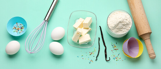 Different ingredients and utensils for baking muffins on turquoise background