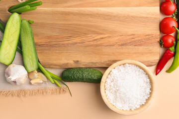 Composition with wooden cutting board, fresh vegetables and bowl of sea salt on color background, closeup