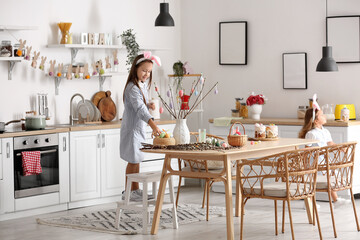Little girl decorating tree branches with Easter eggs in kitchen