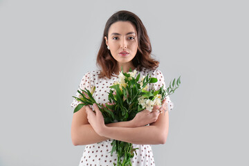 Young woman in dress with alstroemeria flowers on grey background